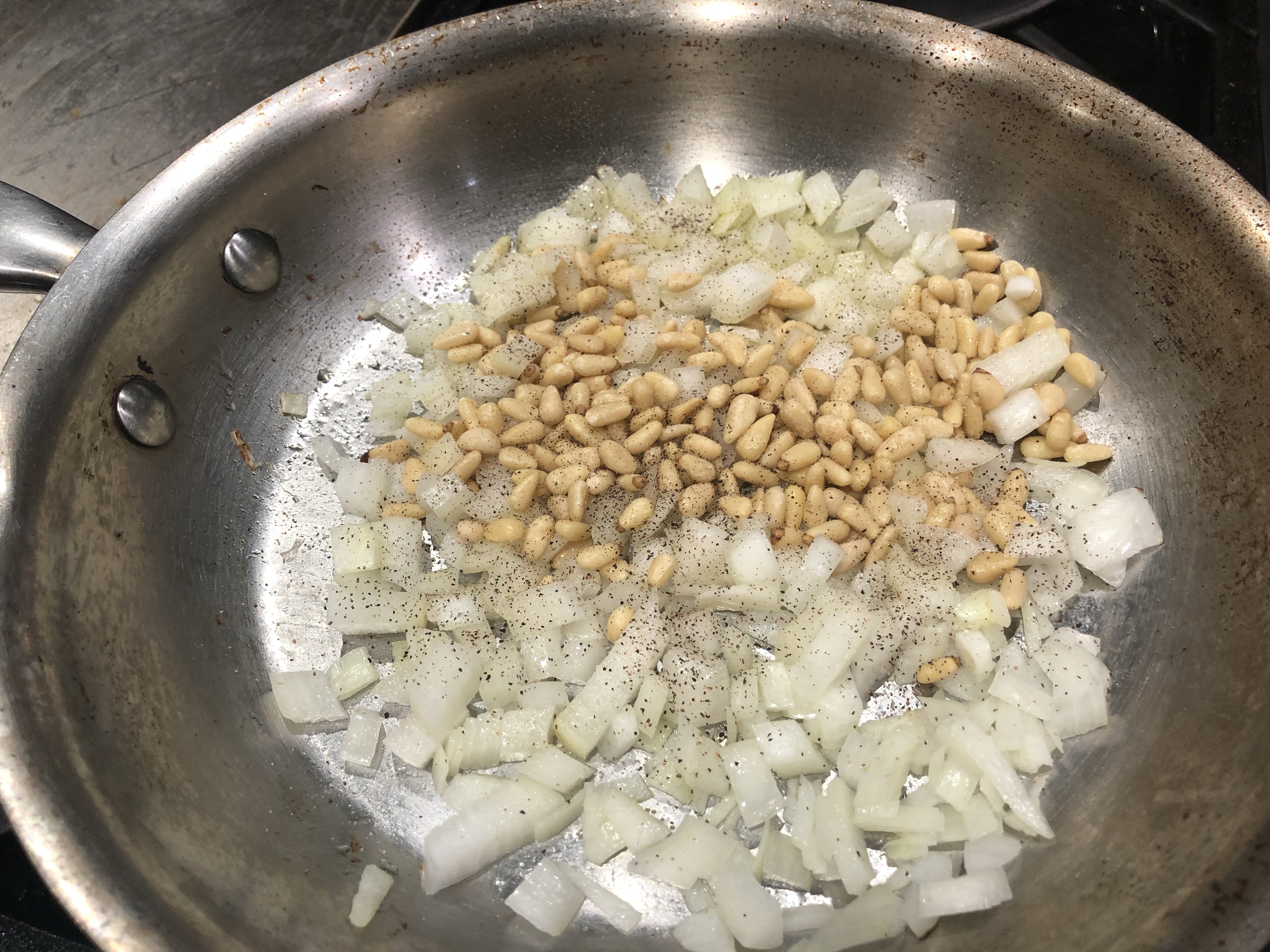 Seasoned onions and pine nuts in sauté pan.